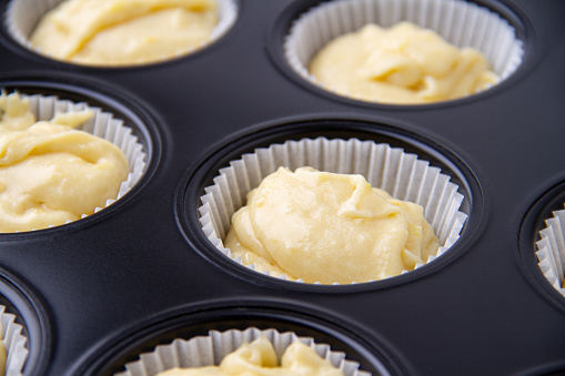 Muffin mold filled with raw yellow dough, close-up