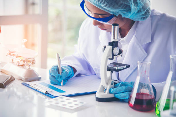 istock Woman scientist hand write note information in medical lab look at science microscope medical test, research biology chemistry. Asian Females technician laboratory analyzing blood test pharmaceutical 1432778221