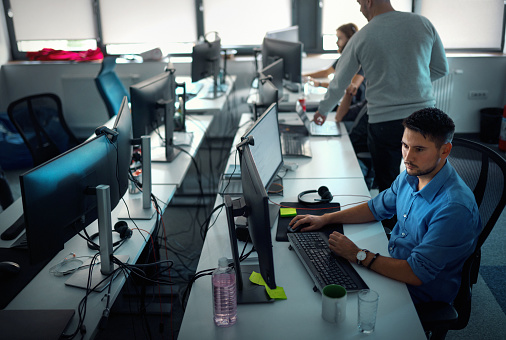 Startup business and entrepreneurship problem solving. Young AI programmers and IT software developers team brainstorming and programming on desktop computer in startup company share office space