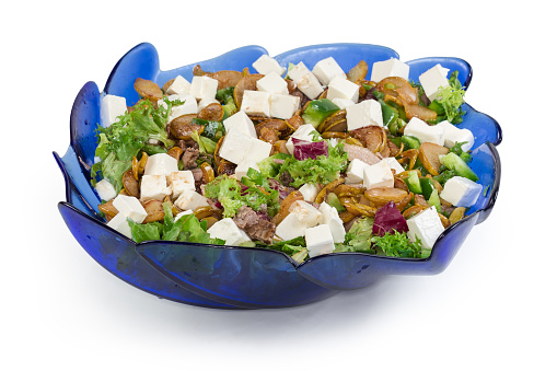 Salad made with boiled duck meat, soft cheese, roasted slices of pear, green bell peppers and leaf lettuce in the blue glass salad bowl on a white background