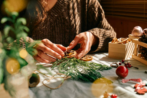 woman making christmas arrangement with fir branches and dried oranges. female hands creating christmas craft handmade decor. new year celebration. winter holidays. - new years eve christmas paper christmas fir tree imagens e fotografias de stock