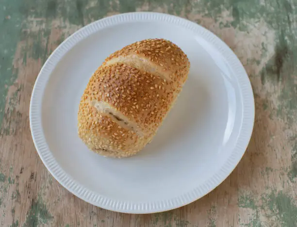 Fresch sasame seed bun from a german bakery served on a white plate isolated on wooden table. Top view