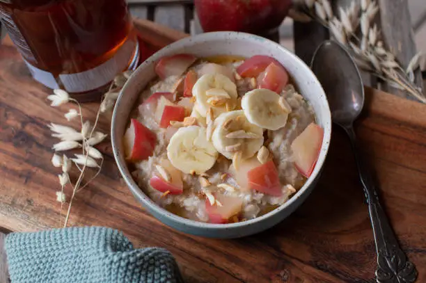 Delicious warm breakfast bowl for autumn and winter season with a fresh cooked oatmeal porridge. Topped with fresh bananas, sauteed apples, almonds and maple syrup.