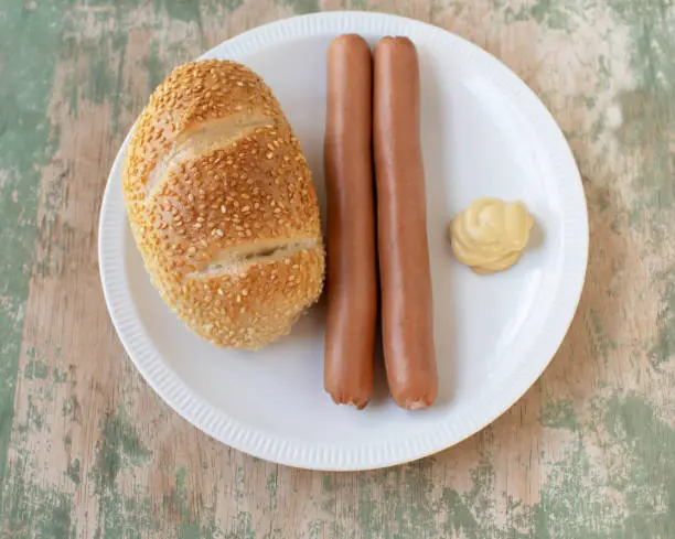 Traditional german fast food meal with vienna sausages, mustard and bun. Served on a plate isolated on wooden table. Top view