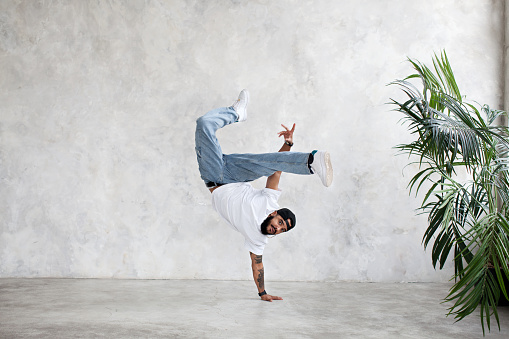 B-Boy performing one handed freeze. Guy breakdancer stands on arm and lifted legs up. Hip hop dance
