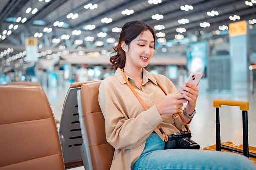 Happy asian tourist woman using mobile smartphone with suitcase traveling between waits for flight in Airport Terminal, Browse Internet, flight check in, Tourist journey trip concept