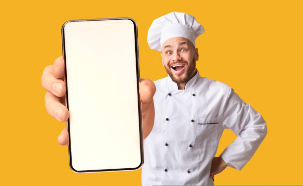 istock Happy chef man showing smartphone with white blank screen, recommending catering service or food delivery app 1432790539
