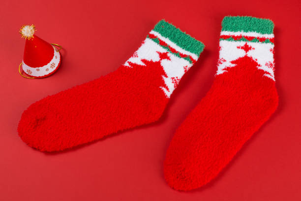 istock Two red Christmas socks, as if walking, next to the Christmas tree, on a red background 1432791327