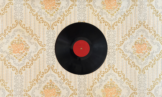 A vinyl record hangs on the wall against the backdrop of old wallpaper.