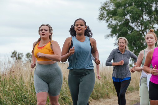 A front-view shot of a group of female friends running outdoors by a field in Northumberland, England.