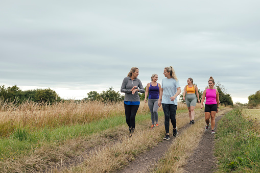 A front wide-view shot of a group of female friends in a running group, they are walking and taking a break outdoors by a field in Northumberland, England.