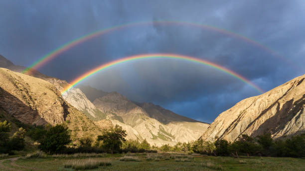 istock Bright full rainbow on the background of storm cloud over mountain range and valley. 1432797112
