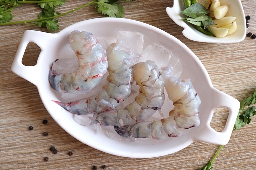 Cleaned, Peeled & Deveined Tiger Prawns or Asian tiger Shrimps. Also known as Kolambi or Bagda chingri. Recipe ingredients like pepper, chilies, garlic, curry leaves at background with copy space.