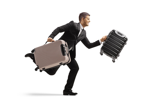 Full length profile shot of a businessman running and carrying suitcases isolated on white background