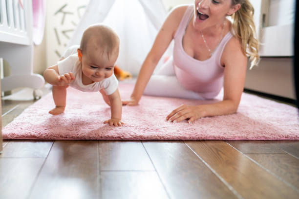 Mother watching proudly as her baby girl crawling on the floor stock photo