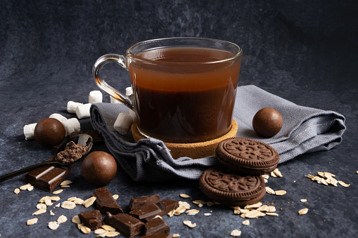 Hot oatmeal cocoa in a transparent mug with cookies and chocolates on a dark background