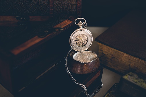 The high-angle view of an antique pocket watch over the box in the darkness