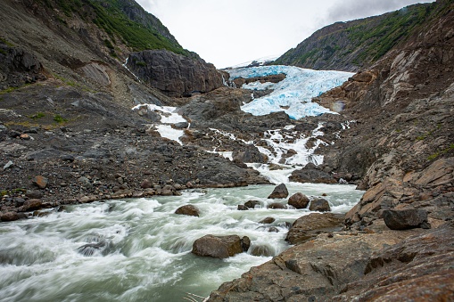 A beautiful landscape of a stream flowing on a rocky slope with glaciers on top