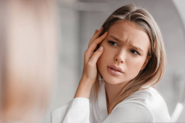 Acne prone skin concept. Sad lady looking at mirror and checking her face skin, standing in bathroom interior Acne prone skin concept. Sad lady looking at mirror and checking her face skin, standing in bathroom interior, selective focus on her reflection cheek stock pictures, royalty-free photos & images