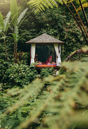 Two massage therapists working in a luxury outdoor spa. View of a massage pavilion surrounded by nature at a serene holiday resort.