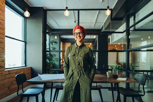 Happy female entrepreneur smiling at the camera while standing in an office boardroom. Cheerful Muslim businesswoman wearing a headscarf in a modern workplace.