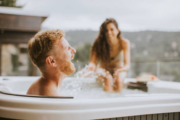молодая пара наслаждается в открытой гидромассажной ванне в отпуске - whirlpool стоковые фото и изображения