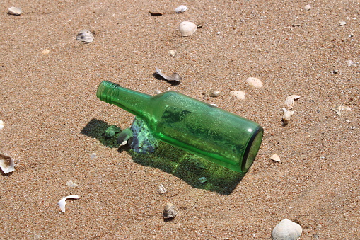 Glass bottle isolated on beach, surrounded by seashells