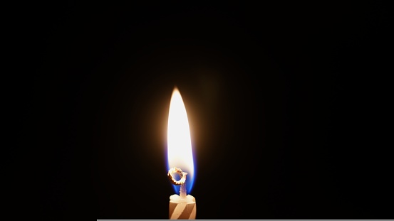 a small striped candle with flames in the dark. combustion process. the concept of belief in God and a symbol of mourning. candles for birthday cake.