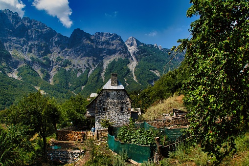 A scenic view of an old building with a garden on the background of mountains against the blue sky