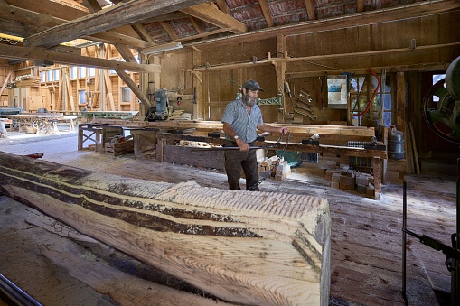 A piece of a log with sawdust on it and a man working in an old sawmill