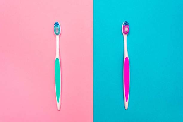 nahaufnahme von blauen und rosa plastikzahnbürsten mit rosa und blauer borste auf rosa und blauem hintergrund - toothbrush pink turquoise blue stock-fotos und bilder