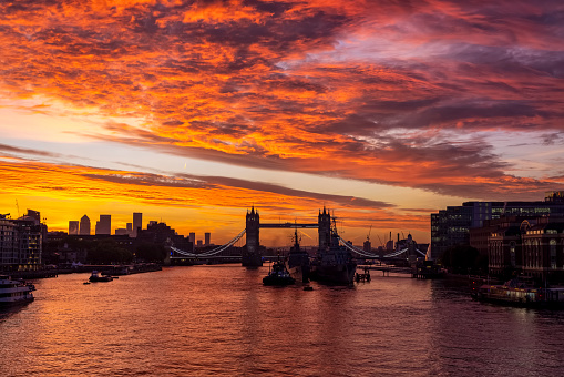 A intense, red sunrise behind the skyline of London, England, with the famous Tower Bridge and River Thames