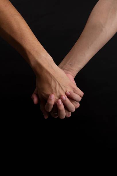 istock Two people holding each other hands on the black background, vertical, close-up 1432830259