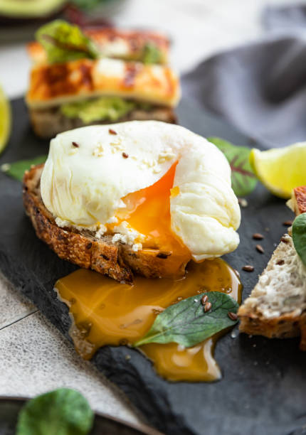 variedad de sándwiches con pan de tartina con huevo escalfado, puré de aguacate y queso a la plancha con hojas de ensalada y lima sobre pizarra. desayuno o brunch saludable. concepto de alimento dietético. - salad breakfast cooked eggs fotografías e imágenes de stock