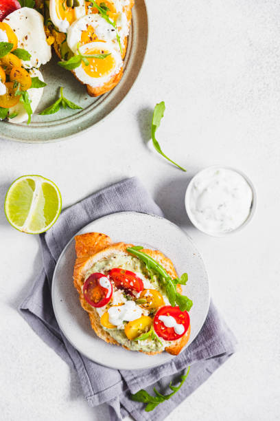 istock Variety of croissant sandwiches with tomato, cucumber, mozzarella cheese, eggs and mashed avocado with mint and arugula. Open savory sandwiches. Tasty healthy breakfast. 1432832621