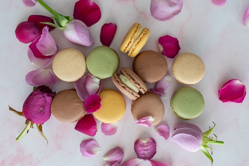 A top of macaroons stacked placed on a white surface next to purple rose petals