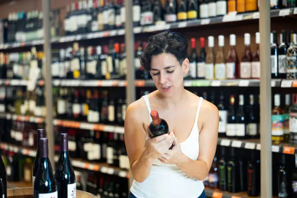 Portrait of young brunette visiting winehouse in search of bottle of good wine
