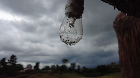A closeup of a glass light bulb with water droplets on a cloudy day outdoors