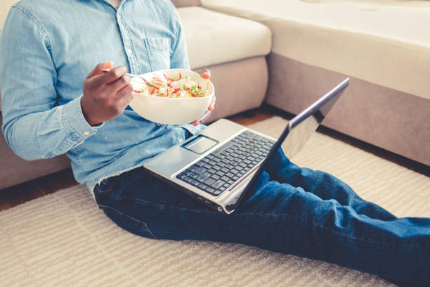 istock Shot of a young man using a laptop and having a salad while working from home. African American young man eating lunch while working on laptop. 1432840920
