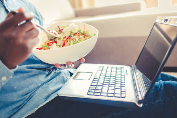 istock Shot of a young man using a laptop and having a salad while working from home. African American young man eating lunch while working on laptop. 1432840924