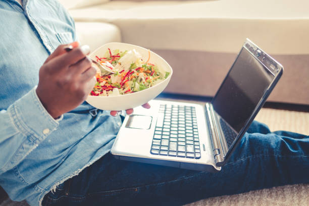 istock Young man relaxing at home, sitting on the floor eating a takeaway meal while working on the laptop at home during the day. 1432841015