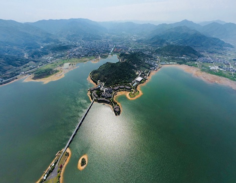 A drone view of shiny blue lake with valley and foggy mountains on horizon under a gray sky