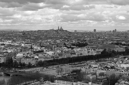 A vintage looking skyline photo taken in Paris France. The Eiffel Tower is to the left of the frame with dramatic clouds in the sky as a background.