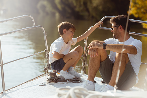 Father and son enjoying a day on the water. They sit on the bow of the ship and talking