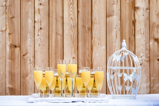 Some glasses of yellow drinks on the table with a white, decorated cell besides, on the wooden background