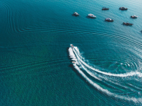 Aerial view of multiple boats on the sea, some anchored in a bay of a Greek island. Spending summer vacations on a sailboat exploring Greece.