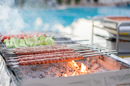 Grill Adana kebab on flaming near resort swimming pool