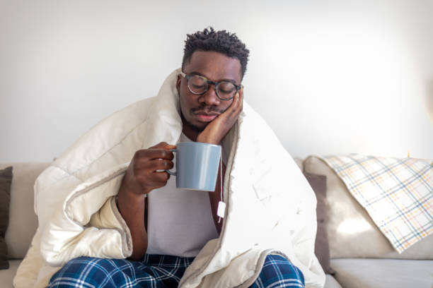 istock Feeling bad. Sick african-american man drinking hot healing tea in bed, touching his forehead, empty space 1432853546