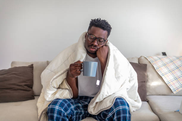 Feeling bad. Sick african-american man drinking hot healing tea in bed, touching his forehead, empty space