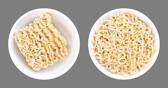 Instant ramen, in white bowls. Dried block of instant noodles, and the same amount of noodles, soaked in boiling water. Isolated, on gray background, macro food photo.